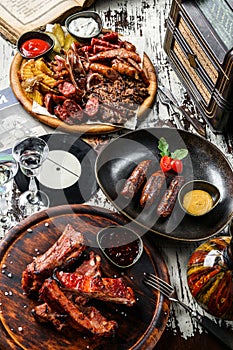 Set of meat dishes, fried sausages on a plate, grilled meat and pig ears with fries potatoes on cutting board, barbecue pork spare