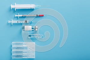 A set of medical syringes and ampoules with medicines and vaccines in a row on a blue background photo