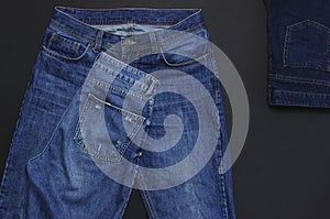 Set of men`s and women`s blue jeans on black background top view flat lay. Detail of nice blue jeans. Jeans texture or denim