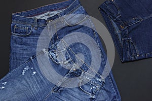 Set of men`s and women`s blue jeans on black background top view flat lay. Detail of nice blue jeans. Jeans texture or denim