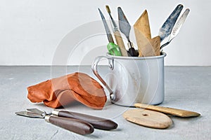 A set of modeling tools in a metal mug and a piece of brown plasticine on a gray stone table. Sculptors workshop a place