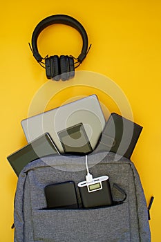 A set of modern gadgets: external battery, laptop, tablet, smartphones are in a fashionable textile backpack. Yellow background.