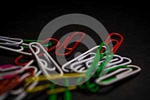 A set of multi-colored office paper clips of plastic are scattered on black monophonic background.