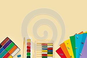 Set of multicolored paints, brushes, plasticine, paper, abacus, buttons and paper clips on  beige background.  School and office