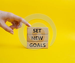 Set New Goals symbol. Wooden blocks with words Set New Goals. Beautiful yellow background. Businessman hand. Business and Set New