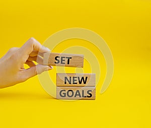 Set New Goals symbol. Wooden blocks with words Set New Goals. Beautiful yellow background. Businessman hand. Business and Set New