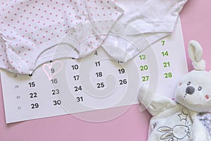 Set of newborn accessories in anticipation of  child - calendar with circled number 9 nine, baby clothes, toys on pink