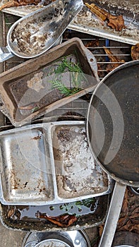 A set of old baking trays dishes and pans in a childs outdoor mud kitchen portrait