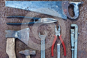 Set of old construction tools: hammer, saw, pliers, etc. on a flat lay background of rusty metal.