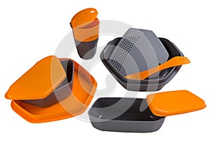 A set of orange plastic dishes for camping or for travel, food containers, plates and spoons, a plastic glass, on a white
