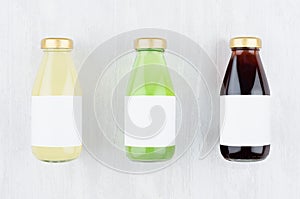 Set of organic fruits juices - pineapple, kiwi, pomegranade in glass bottles with blank label on white wood background, mock up.