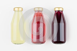 Set of organic fruits juices - pineapple, strawberry, pomegranade in glass bottles on white wood background, mock up for design.