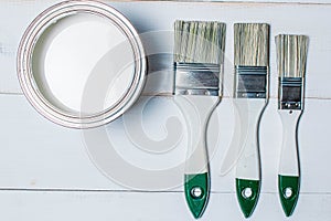 A set of paint brushes and a jar with white paint on a textured wood table painted white