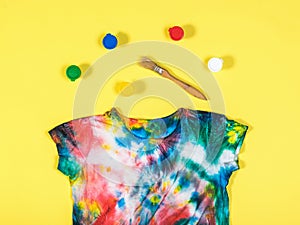 A set of paints and a tie dye t-shirt on a yellow background. Flat lay.