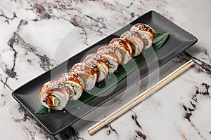 Set of philadelphia rolls with eel, smoked salmon, avocado and green bamboo leaf in a black ceramic plate with chopstick on a