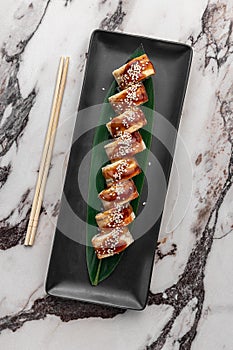 Set of philadelphia rolls with eel, smoked salmon, avocado and green bamboo leaf in a black ceramic plate with chopstick on a