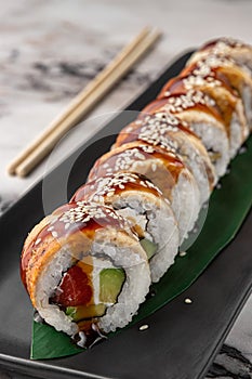 Set of philadelphia rolls with eel, smoked salmon, avocado and green bamboo leaf in a black ceramic plate with chopstick on a