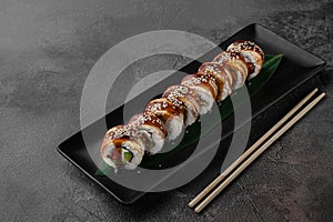 Set of philadelphia rolls with eel, smoked salmon, avocado and green bamboo leaf in a black ceramic plate with chopstick on a dark