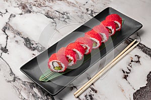 Set of philadelphia rolls with red flying fish caviar, avocado, salmon and green bamboo leaf in a black ceramic plate with