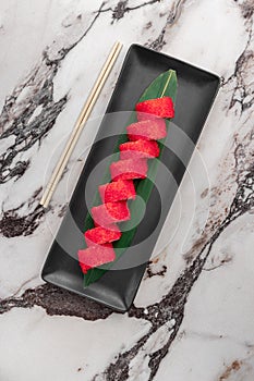 Set of philadelphia rolls with red flying fish caviar, avocado, salmon and green bamboo leaf in a black ceramic plate with