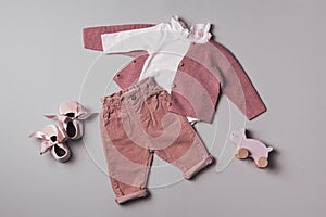Set of pink clothes and accessories fot newborn girl. Toys, bodysuit, jeans, knitted cardigan on grey backgroundd. Mock