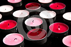 A set of pink tealight paraffin candle lying on a black background