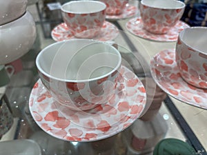 A set of pink and white cups and saucers are displayed on a glass shelf