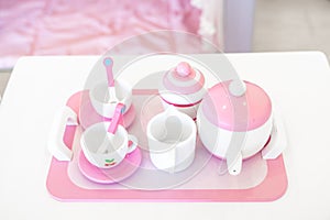 A set of pink white pastel color wood  toy tea cups including 2 coffee cups with teaspoons, a teapot, a sugar jar  and a milk jug