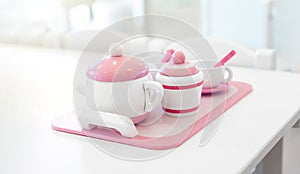 A set of pink white pastel color wood  toy tea cups including 2 coffee cups with teaspoons, a teapot, a sugar jar  and a milk jug