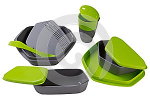 A set of plastic dishes for camping or for travel, green, food containers, plates and spoons, a plastic glass, on a white