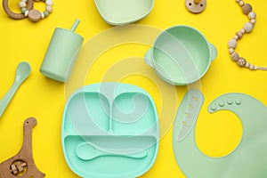 Set of plastic dishware and baby accessories on yellow background, flat lay