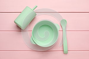 Set of plastic dishware on pink wooden background, flat lay. Serving baby food