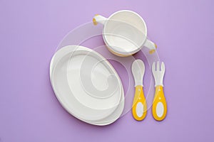 Set of plastic dishware on violet background, flat lay. Serving baby food