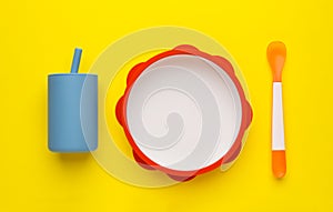 Set of plastic dishware on yellow background, flat lay. Serving baby food