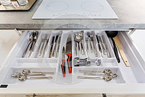 Set of plates, cups, knives, forks and wine glasses on the shelf in the kitchen cabinet