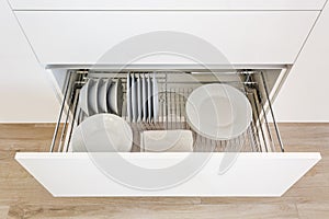 Set of plates, cups, knives, forks and wine glasses on the shelf in the kitchen cabinet