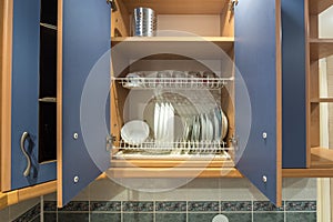 Set of plates, cups, knives, forks and wine glasses on the shelf in the kitchen cabinet