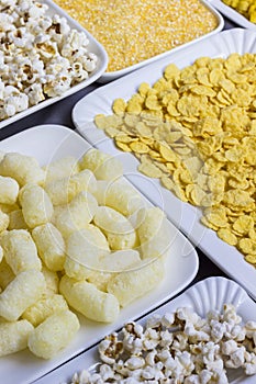 A set of products made from corn: popcorn, sticks, cereal, and corn grits. White plates