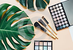Set of professional decorative cosmetics, makeup tools and accessory on yellow background with big monstera leaf. Beauty, fashion