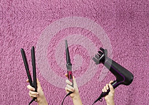Set of professional hair tools against pink fluffy background.Woman holding hair dryer,hair iron and curling one.Empty space