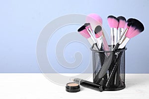 Set of professional makeup brushes in holder on white wooden table. Space for text