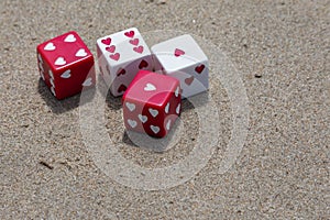 Set of red and white dice with hearts thrown on the sand at the beach