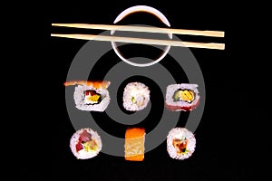 A set of rolls of different kinds with soy sauce and sushi sticks isolated on a black background