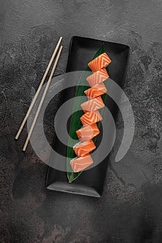 Set of rolls philadelphia kappa and green bamboo leaf in a black ceramic plate with chopstick on a dark gray textured background,
