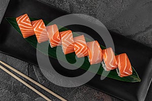 Set of rolls philadelphia kappa and green bamboo leaf in a black ceramic plate with chopstick on a dark gray textured background,