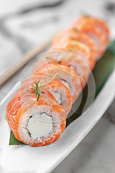 Set of rolls philadelphia kappa with microgreens and green bamboo leaf in a white ceramic plate with chopstick on a bright