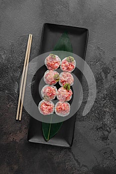 Set of rolls with salmon, red flying fish caviar and green bamboo leaf in a black ceramic plate with chopstick on a dark gray