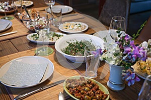 Set rustic wooden table with various homemade salads and appetizers for a casual convivial evening dinner with friends or family,