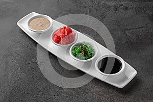 Set of sauces for sushi on a white plate, ginger, soy, sesame, seaweed. dark gray textured background, side view