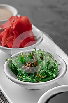 Set of sauces for sushi on a white plate, ginger, soy, sesame, seaweed. dark gray textured background, side view, close-up